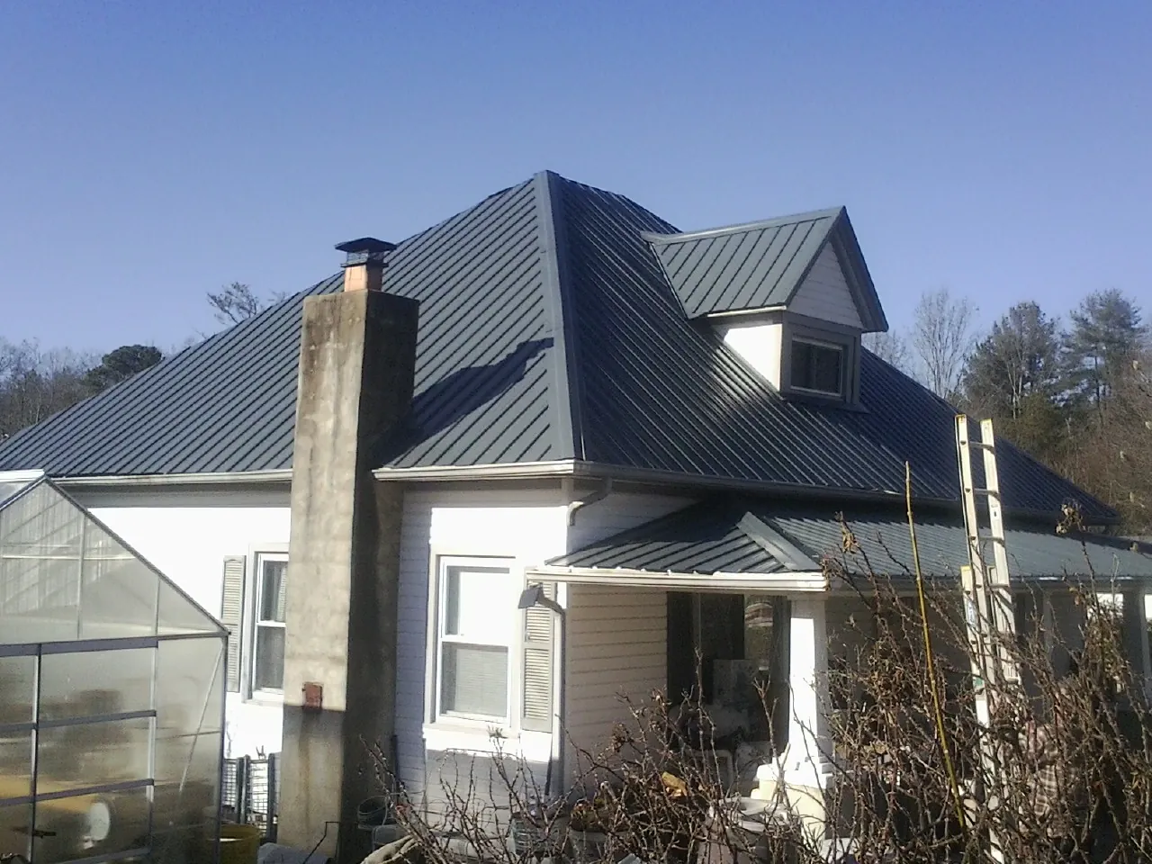 Dark blue standing seam metal roof on a white farmhouse with dormer — Slate & Tile Roof Repair by Roofing Brothers in Grand Forks Afb