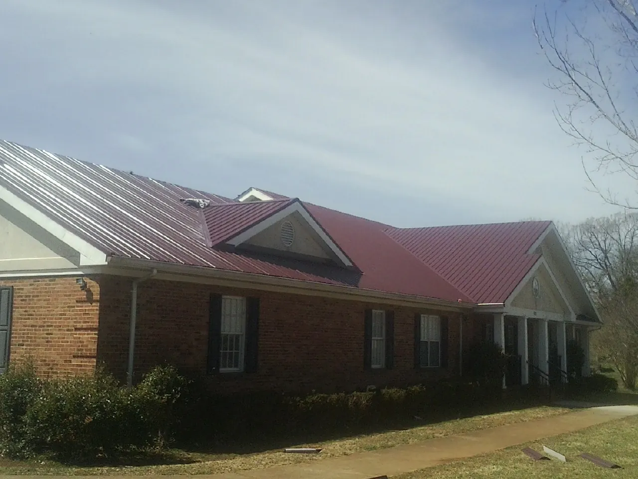 Red metal roof with gabled entries on a long brick building, from a Hail Damage Roof Repair job in Grand Forks Afb