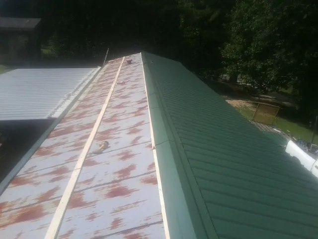 Old rusted panels beside newly installed green metal roofing — Wind Damage Roof Repair by Roofing Brothers in Grand Forks Afb