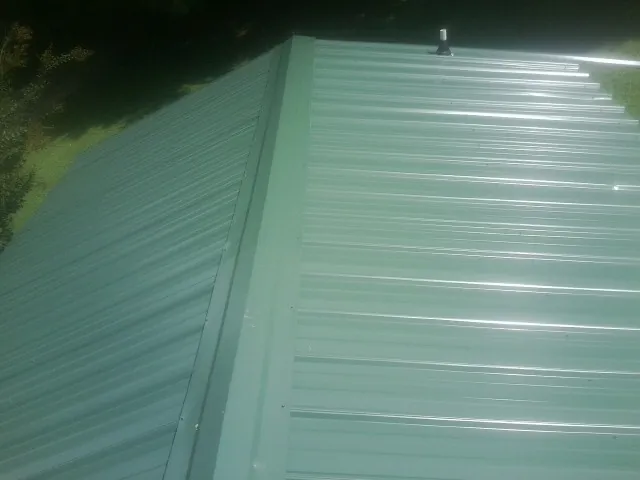 New green metal panels meeting at the ridge of a roof — Flat Roof Repair work by our crew in Grand Forks Afb