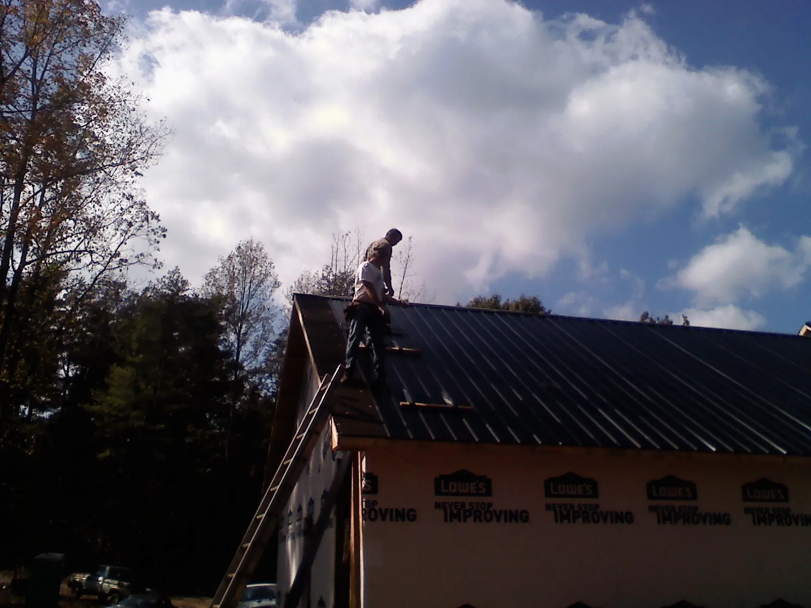Roofer fastening dark metal panels high against a cloudy sky, from a Roof Inspection job in Grand Forks Afb
