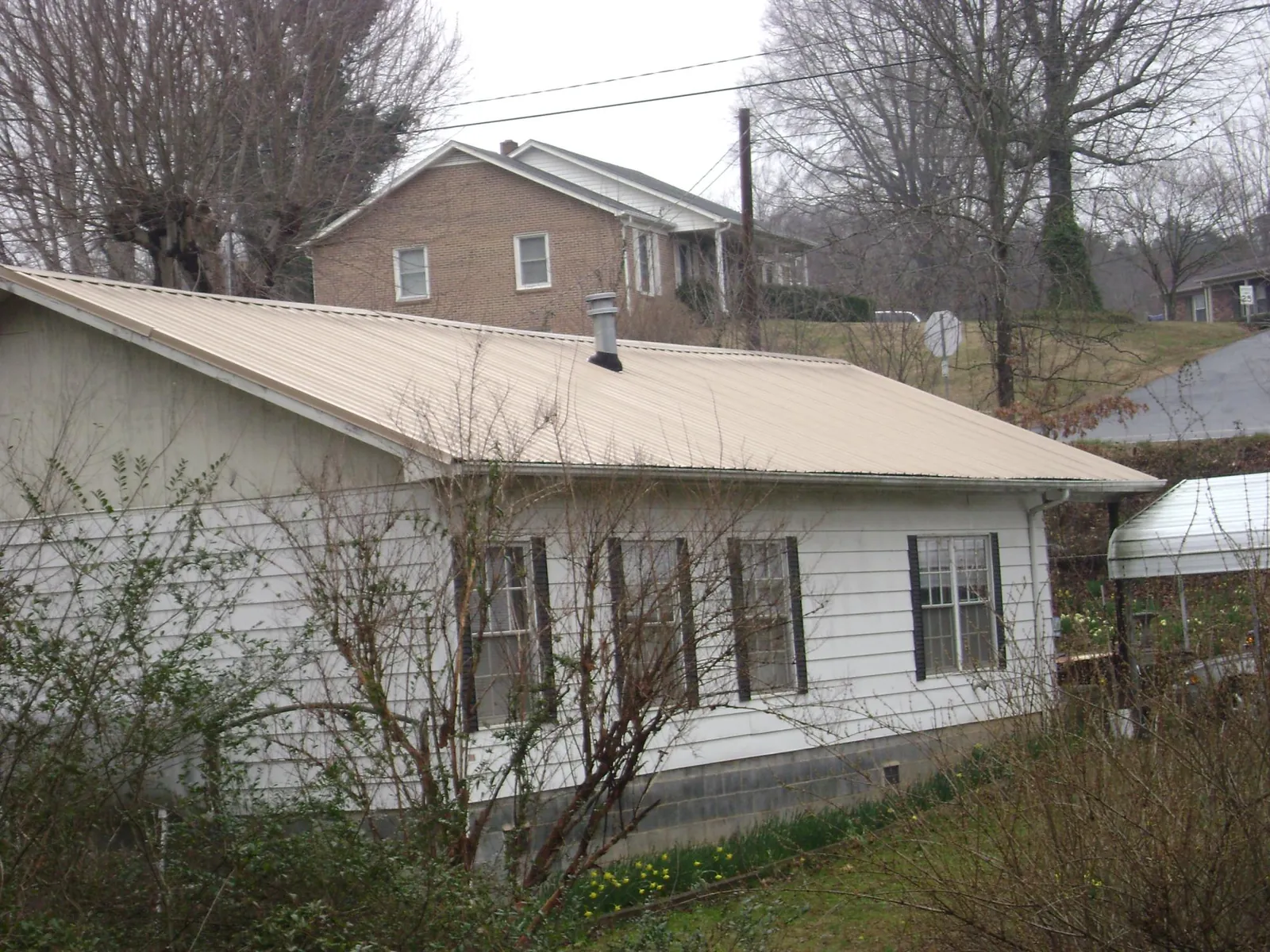 Tan metal roof on a white sided house set into a hillside — Commercial Roofing by Roofing Brothers in Grand Forks Afb